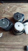 Three fly reels in their protective cases on wooden surface showing overall lot.