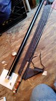 Disassembled rod sections laid beside metal tube and fabric bag on wood floor
