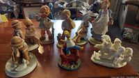 Full view of nine collectible figurines including Holly Hobbie girls, Gretchen Collection, Avon boy with dog, and Homer Snow Babies bears and children.