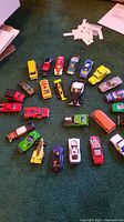 Photo showing assortment of 26 Hot Wheels vehicles laid out on carpet, various colors and models