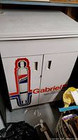 Front view of white metal Gabriel Shock Absorbers cabinet with logo on doors, showing condition and graphic detail.
