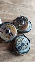 Three Orvis Battenkill fly reels with zippered cases on wooden surface