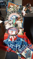 Photo shows Phillies memorabilia including a round dart board, multiple player posters, a Phillies clock, and a red and blue Phillies flag with World Series Champions 2008 text.