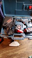 Full set showing Bosch power drill, two batteries, charger, extra drill bits inside carrying case on wooden surface