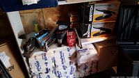 Photo showing multiple staplers, boxes of staples, and lidded plastic case stored on shelf in shed environment.