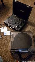 Photo showing both turntables: Memorex 2650MMO USB turntable with warning labels on underside; Polaroid portable turntable in carry case with cover closed