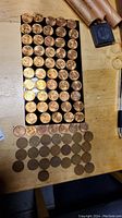 Rows of 81 Wheat Pennies mostly uncirculated on black trays with some coin wrappers visible.