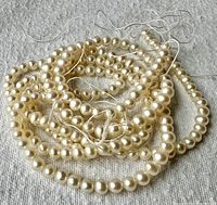 Two 16-inch strands of ivory pearl beads displayed coiled on fabric background.