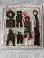 Set of six ancient Chinese coin replicas arranged on branded paper backing, showing round and knife-shaped coins with various inscriptions and holes.