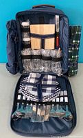 Photo of the opened picnic backpack showing inside contents: cutting board, cheese cutter, salt and pepper shakers, wine glasses, and cutlery.