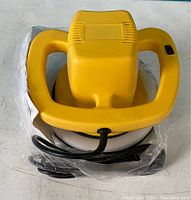 Yellow handheld car polishing and buffering machine with dual handles, black power cord, and circular buffing pad visible. Wrapped partially in plastic.