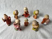 Eight mini Kung-Fu monk figurines arranged on light fabric background showing various poses and colors, detailed facial features visible.