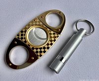 Photo of gold-tone double guillotine cigar cutter showing checkered pattern and dual blades.
