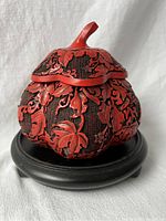 Front view of vintage Chinese red cinnabar carved melon gourd shaped trinket box on a round black wooden stand.