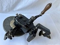 Angle view of vintage hand crank bench grinder showing wood handle and grinding stone.