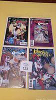 Four Harley Quinn comic books arranged on a yellow surface, showing full front covers.
