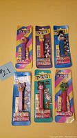 Photo showing front view of six Pez dispensers in original packaging with colorful backing cards, each with a different character head.