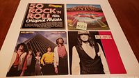 Four vinyl records displayed on a wooden surface showing front covers of '50 Rock 'n Roll Hits', Boston, Air Supply, and Kim Mitchell albums.