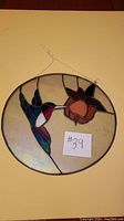 Full view of round stained glass piece with hummingbird and flower design, showing hanging wire and overall condition.