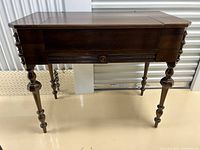 Desk closed with top folded up, showing spool-turned legs and carved apron details.