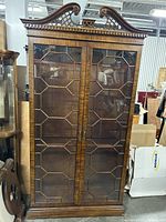 Full front view of vintage wood display cabinet with two decorative glass doors and carved top