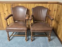 Front-facing photo of two vintage brown leather armchairs, showing overall shape, size and condition of leather and wood frames.