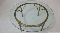 Top down view of round glass coffee table showing clear glass top and metal base with curved support structure.