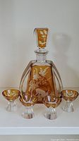 Decanter with stopper center, surrounded by 4 matching amber Bohemian crystal liquor glasses.