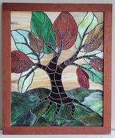 Front view of stained glass artwork showing multicolored leaves and a tree trunk inside a wooden frame.