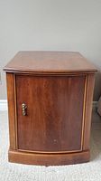 Front view of vintage wooden end table with closed cabinet door and metal handle.