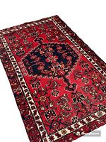 Red bordered Zanjan rug with detailed geometric and floral motif, navy blue center medallion shown at angle