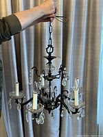 Full view of antique chandelier held by chain, showing four candle lights, crystal prisms, and black painted metal body.