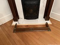 Copper fireplace surround frame placed on wooden floor in front of marble and cast iron fireplace insert.