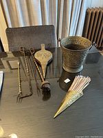 Full set of antique fireplace tools including tongs, poker, brush, shovel, brass bucket, and brass match holder cone with matches arranged on a table.