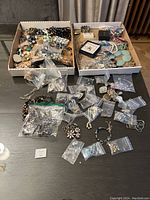 Full view of two boxes and multiple plastic bags containing assorted costume jewelry pieces of different styles and colors.