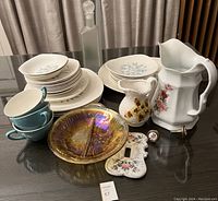 Full assortment of dishes and serveware displayed on table, highlighting floral patterned plates, pitchers, cups, and iridescent glass dish