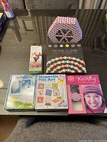 Overview photo of all six items included in the lot arranged on a table, showing unopened packaging of games and craft kits