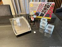 Photo showing the Wilton Mini Treat Pan Set box, stainless steel tray, penguin ceramic mug with lid, and two square glass containers with lids on a table.