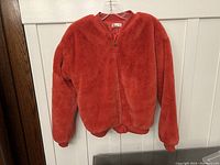 Front view of the red faux fur coat hanging showing zipper closure and ribbed collar and hem.