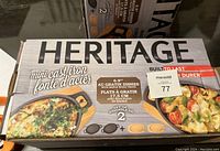Boxed Heritage brand mini cast iron dishes with maple wood trays, 6.9 inches in size, set of 2 per box, with food images on box.