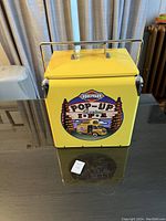 Full view of yellow metal cooler with metal handle, showing front graphics.