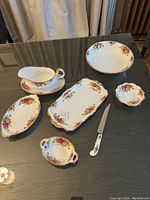 Full set displayed on table with all seven pieces visible including gravy boat with dish, rectangular dish and tray, two small dishes, oval dish and serving knife.