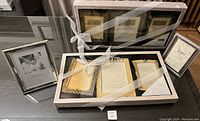 Photo showing multiple silver-tone photo frames, including 3 boxed frames tied with a white ribbon and other loose frames around them on a table