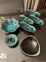 Photo showing entire lot including six teal glazed bowls and dishes and one dark bowl with teal rim.