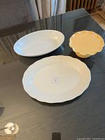 Two white oval platters and one yellow ceramic cake stand on black reflective surface.