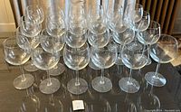 Front view of 24 clear wine glasses arranged in rows on a dark surface, showing shape and quantity.