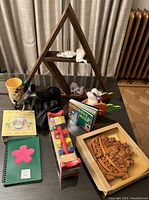 Assorted baby toys and items arranged on a table including a wooden display shelf, plush toys, wooden toys, a book, a notebook, and a decorative mug.