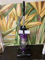 Front view of upright vacuum cleaner with clear dust container labeled Aeroswift and handle attached.