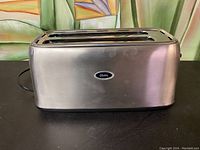 Front and side view showing the toaster's brushed stainless steel finish and Oster logo