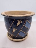 Front view of the round ceramic plant pot showing dark blue glazed exterior with gold and beige leaf and lattice design, and unglazed rim.